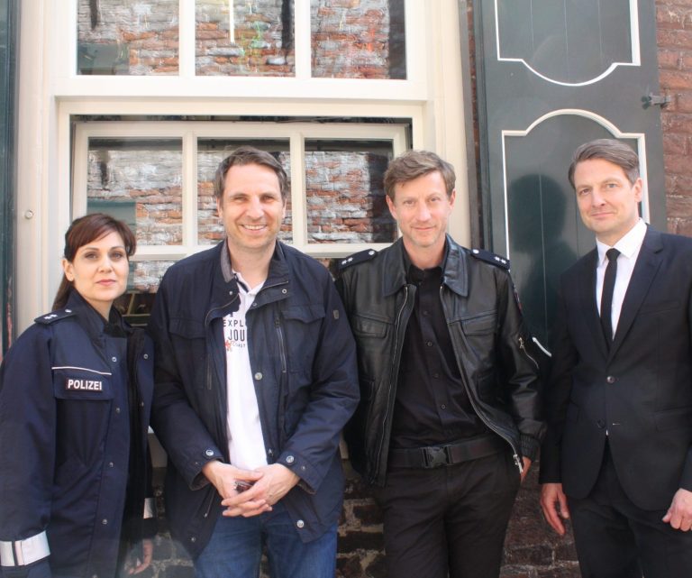 Vier Personen, drei in ihren Filmkostümen, stehen vor einem Backsteinmauerfenster in der Altstadt von Leer.