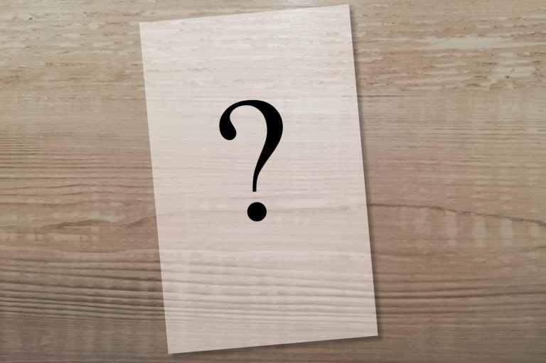 Hölzerner Hintergrund mit einer rechteckigen Fläche, auf der ein schwarzes Fragezeichen prangt.